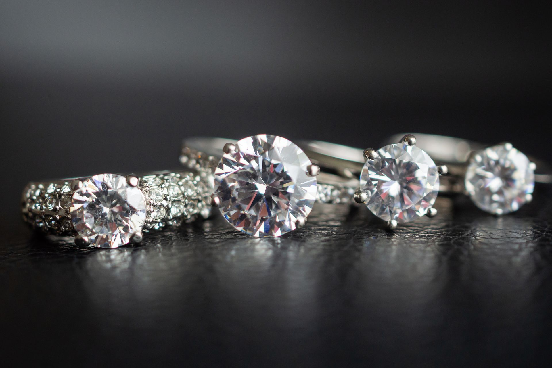 Four diamond engagement rings on a dark surface, varying in size and style.
