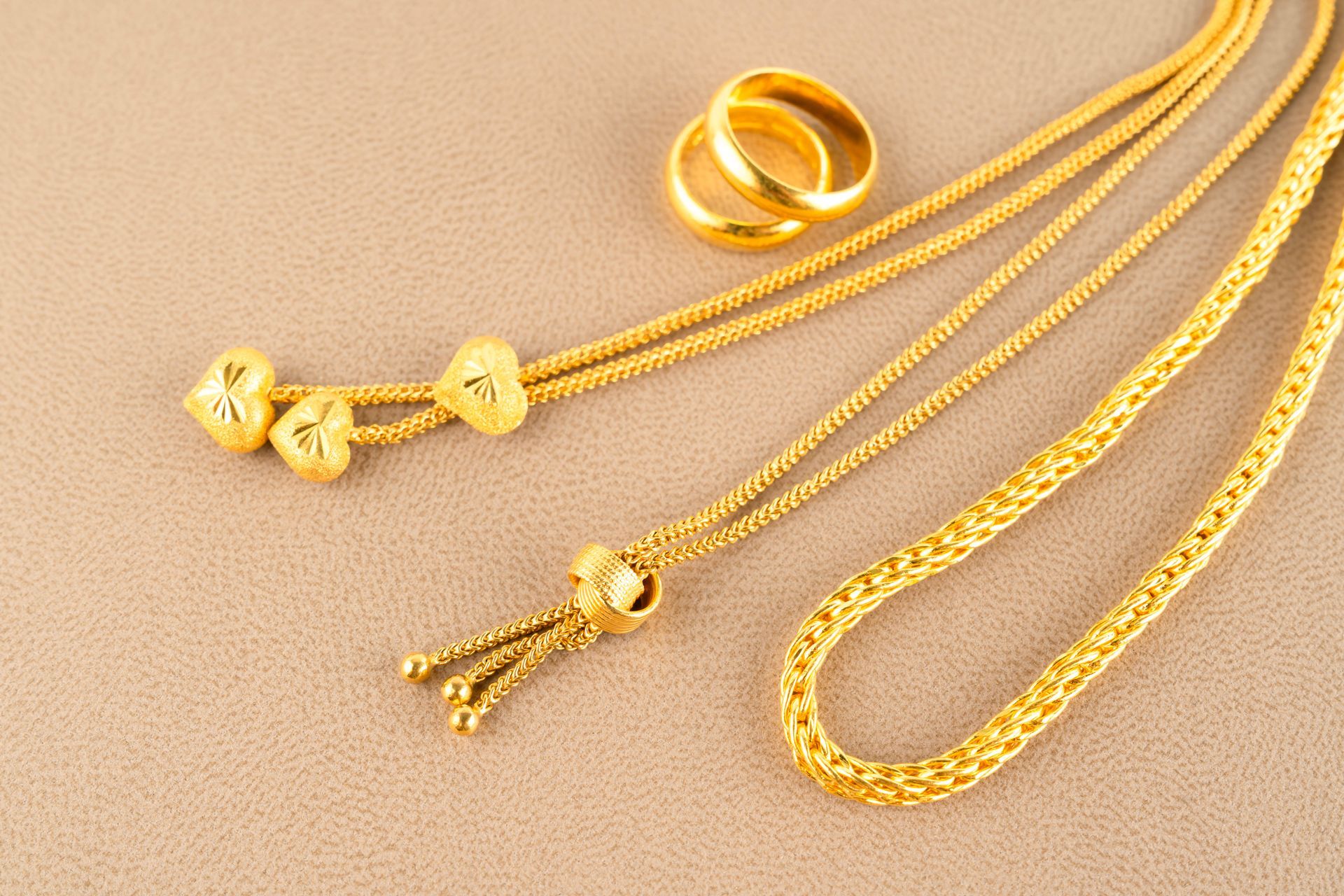 Gold jewelry: two necklaces and two rings on a neutral surface.