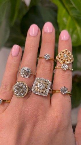 Hand holding a collection of diamond rings with various settings on a background of green leaves.