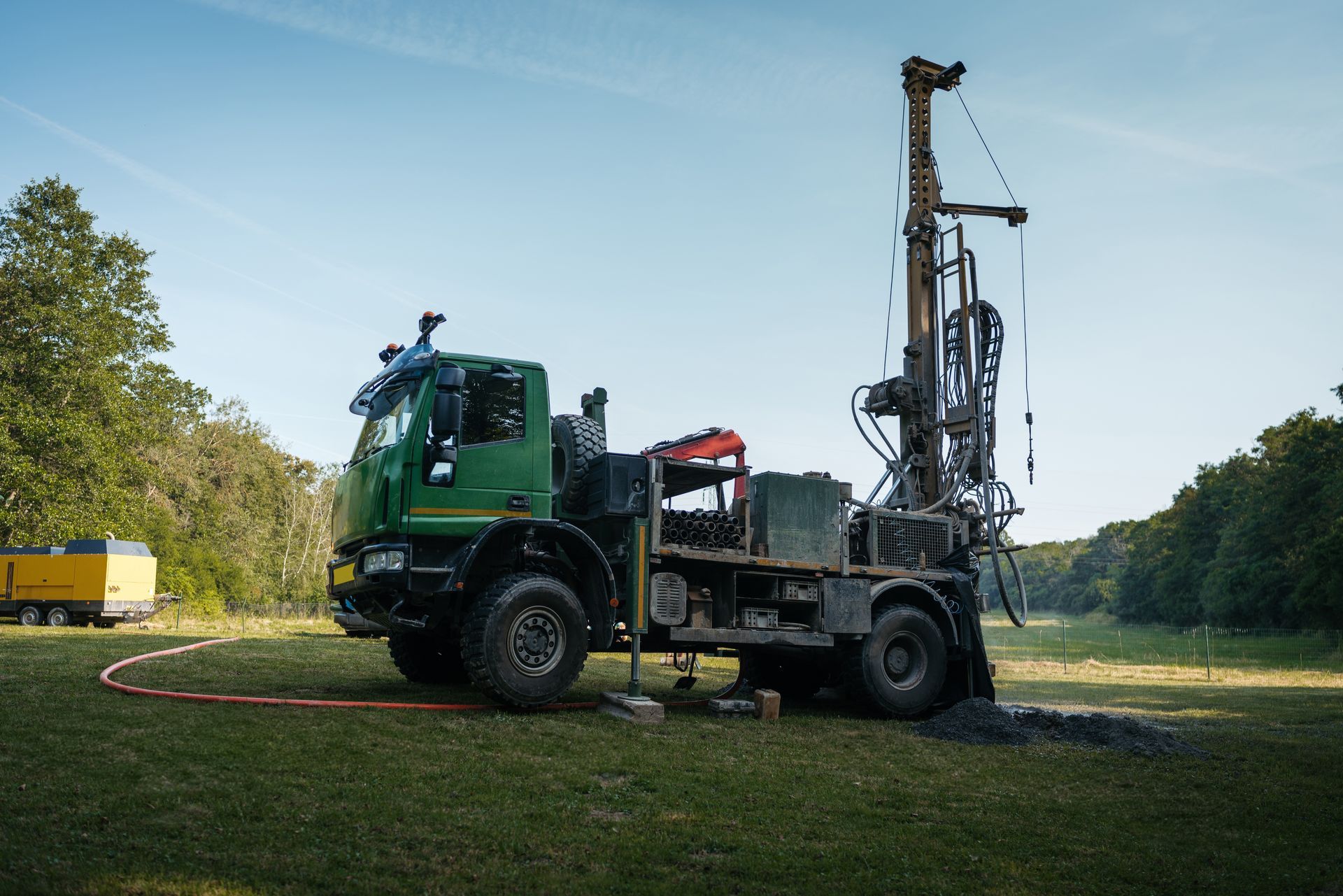 A green truck with a drilling rig attached to it is parked in a grassy field.