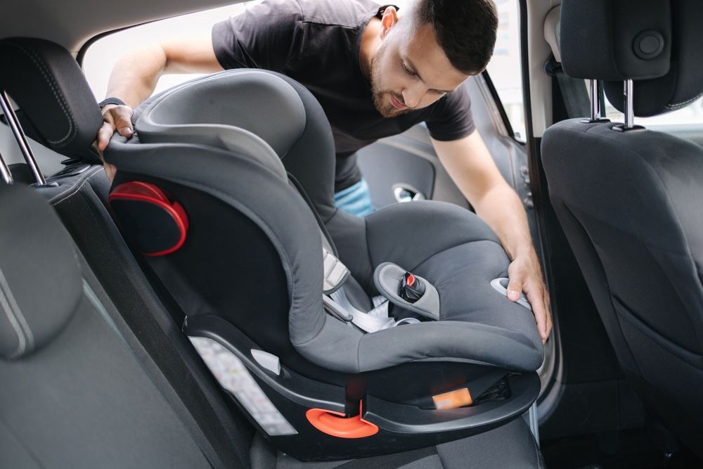 A man is adjusting a car seat in the back seat of a car.
