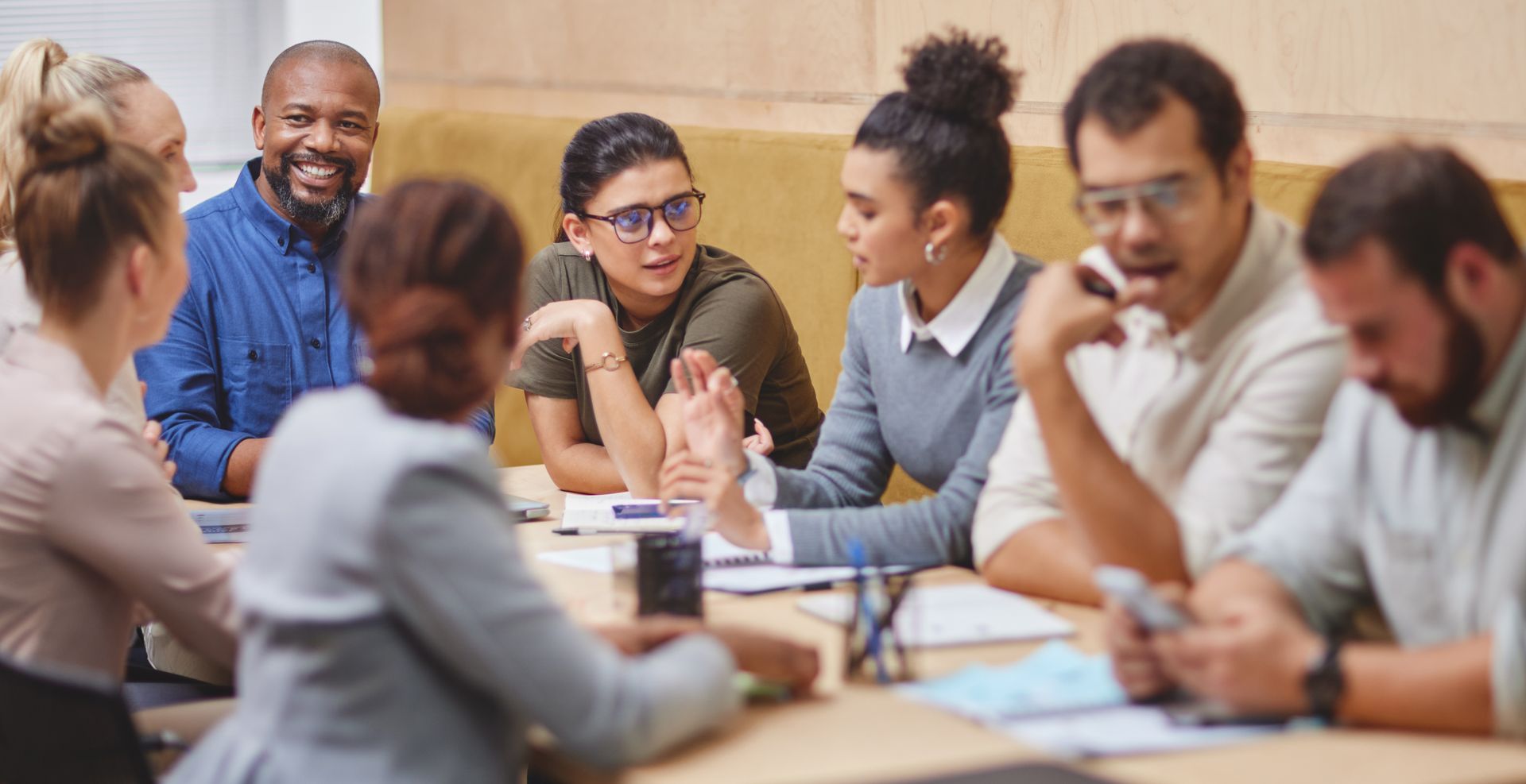 Group of people in an office meeting, discussing and gesturing at a table.