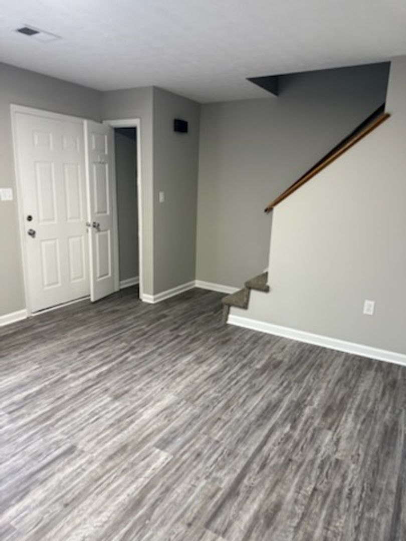 Row of tan townhouses with green doors and shutters; a white car parked on the grass.