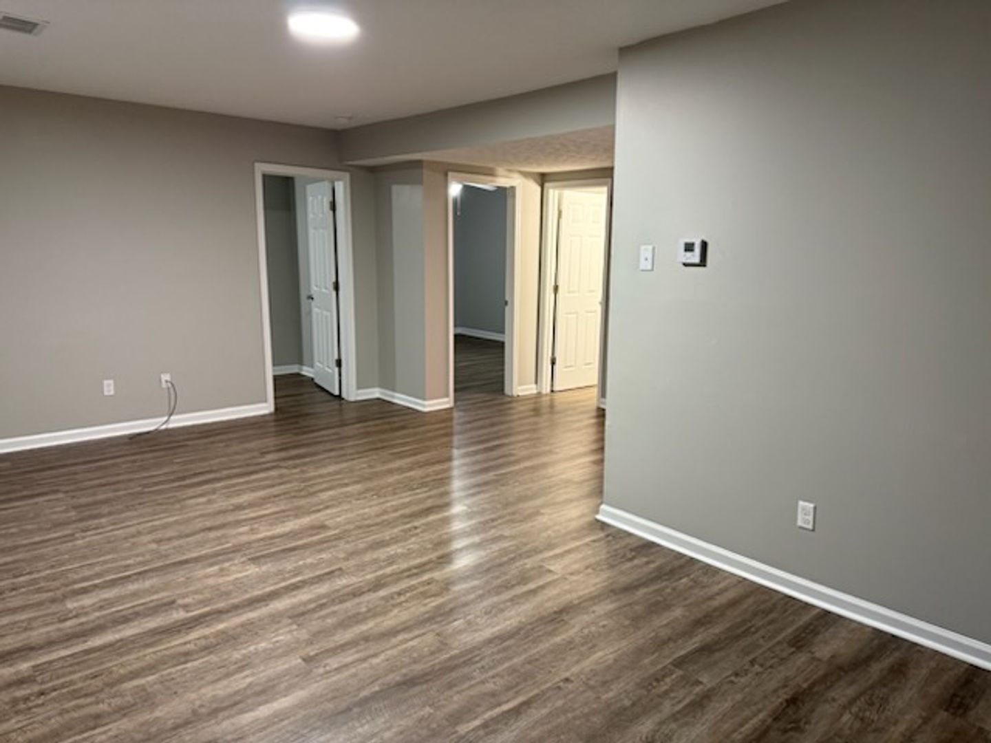 Empty, bright room with white walls, window, radiator, and light wood floors. Opening to a second room.