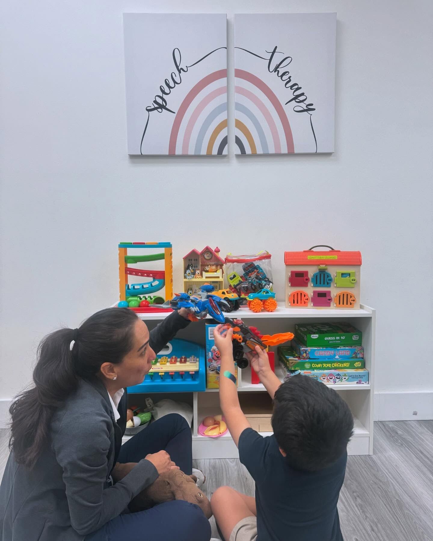 A woman is sitting on the floor reading a book to a boy.