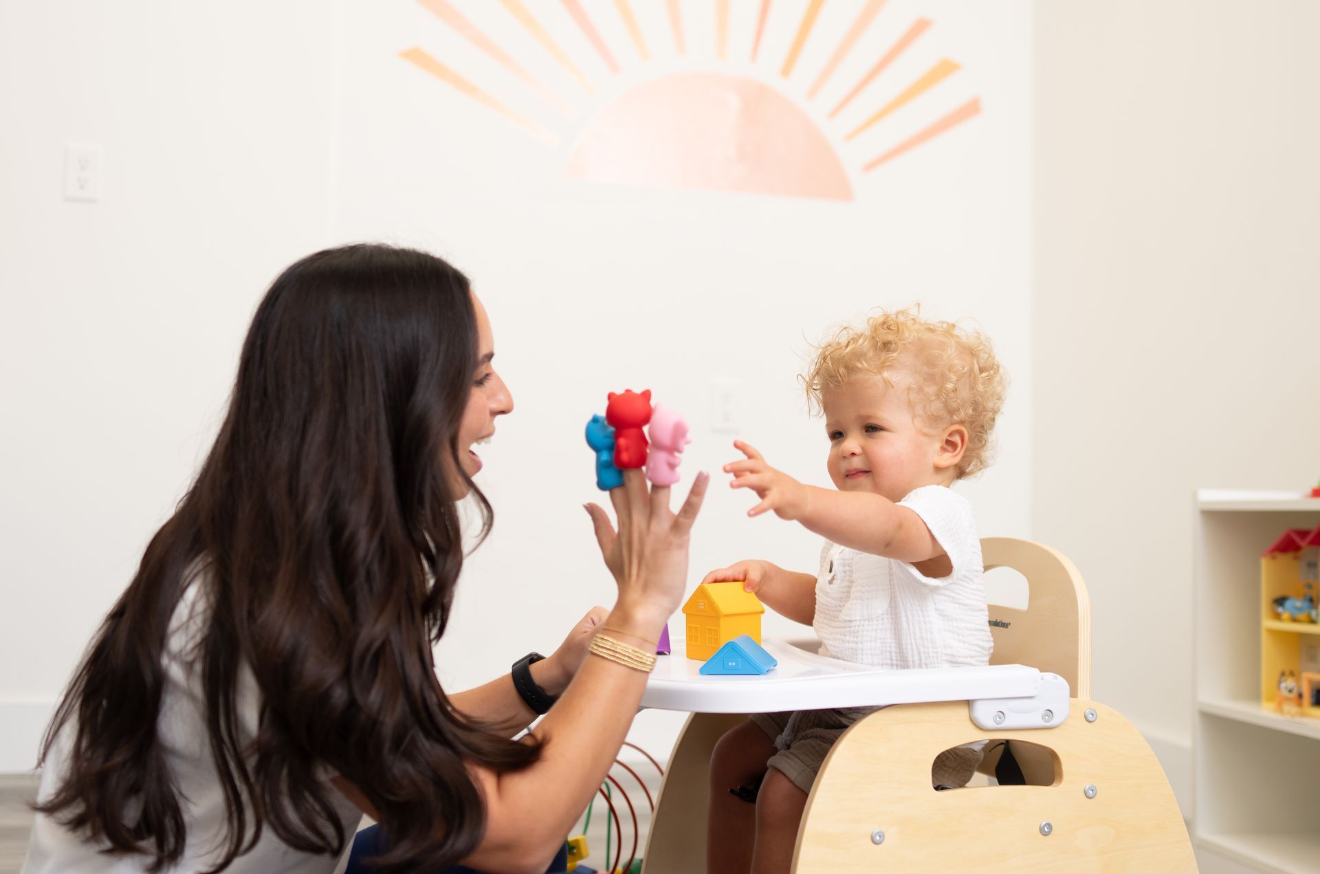 A woman is playing with a baby in a high chair.
