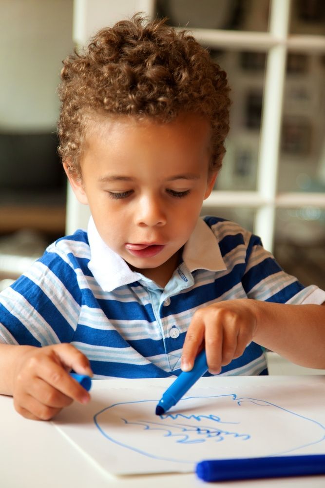 A young boy in a blue and white striped shirt is drawing with a blue marker