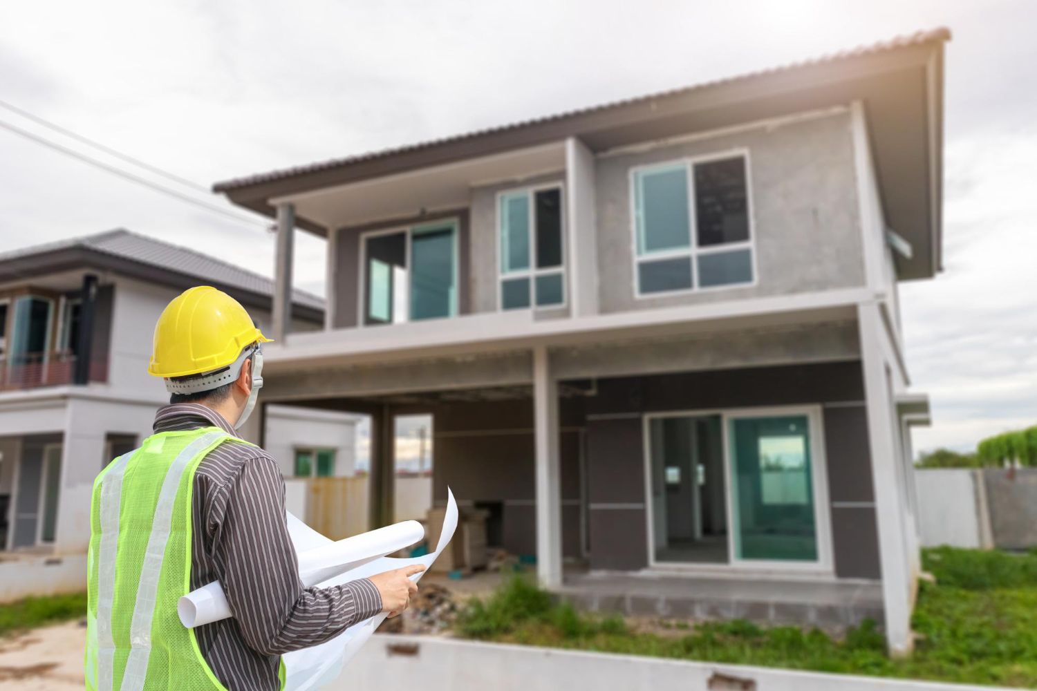 A construction worker is looking at a blueprint of a house under construction.