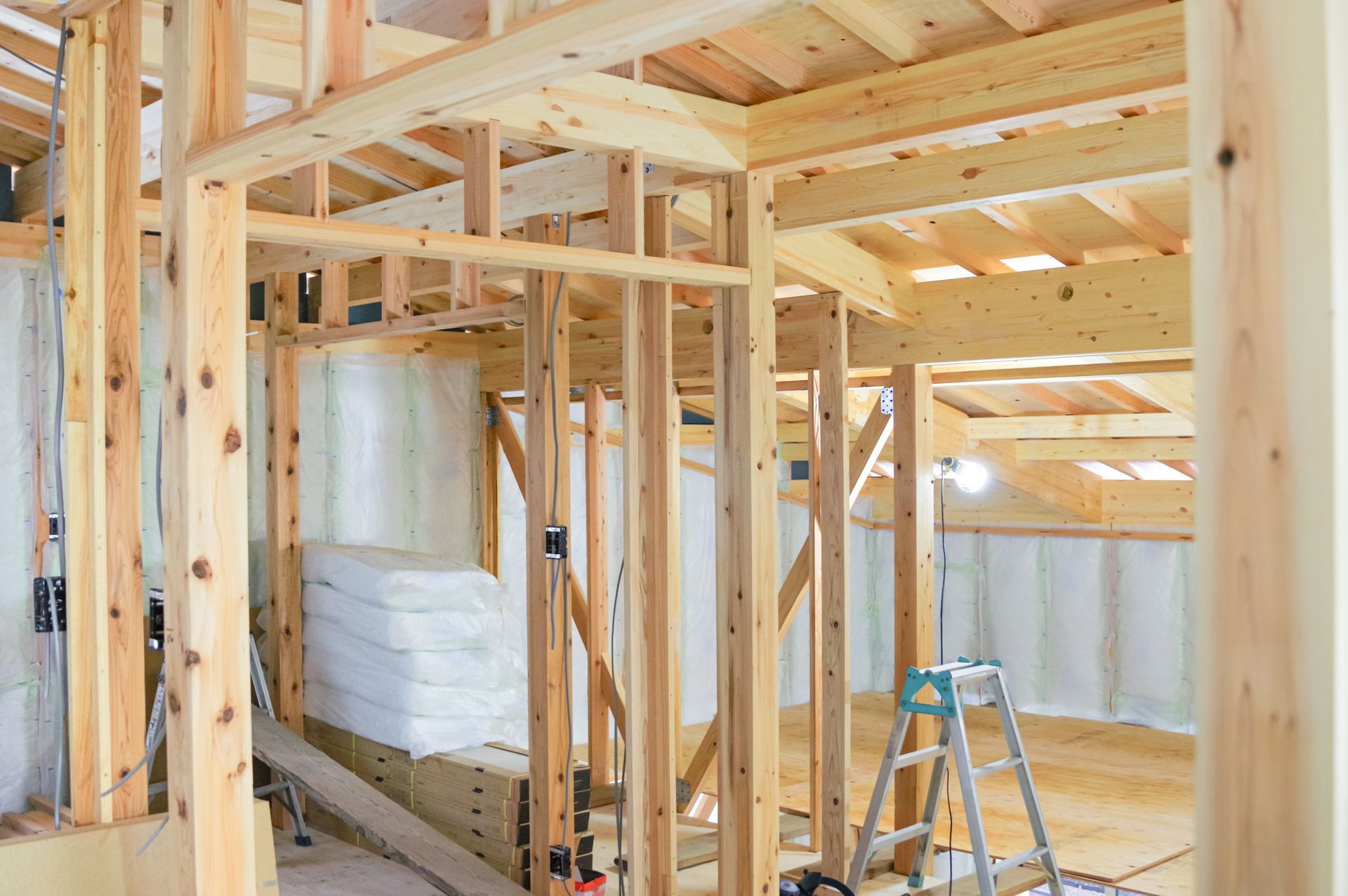 The interior framework of an unfinished wooden house showing exposed studs, support beams, and a ladder.