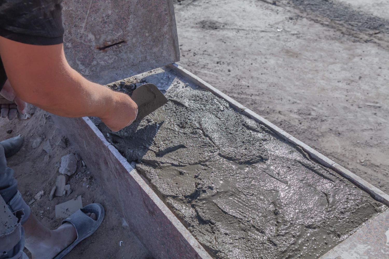 A person is pouring concrete into a container with a spatula.