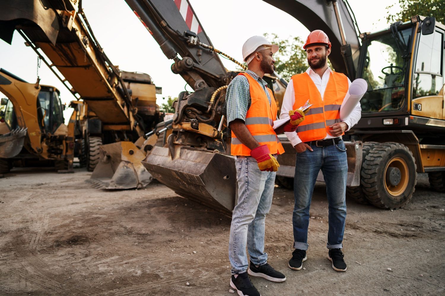 Two construction workers are standing in front of a bulldozer on a construction site.