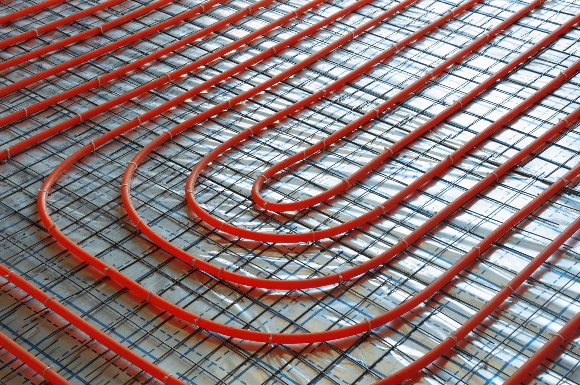 Red pipes in a looped pattern, part of an underfloor heating system, installed on a reflective surface.