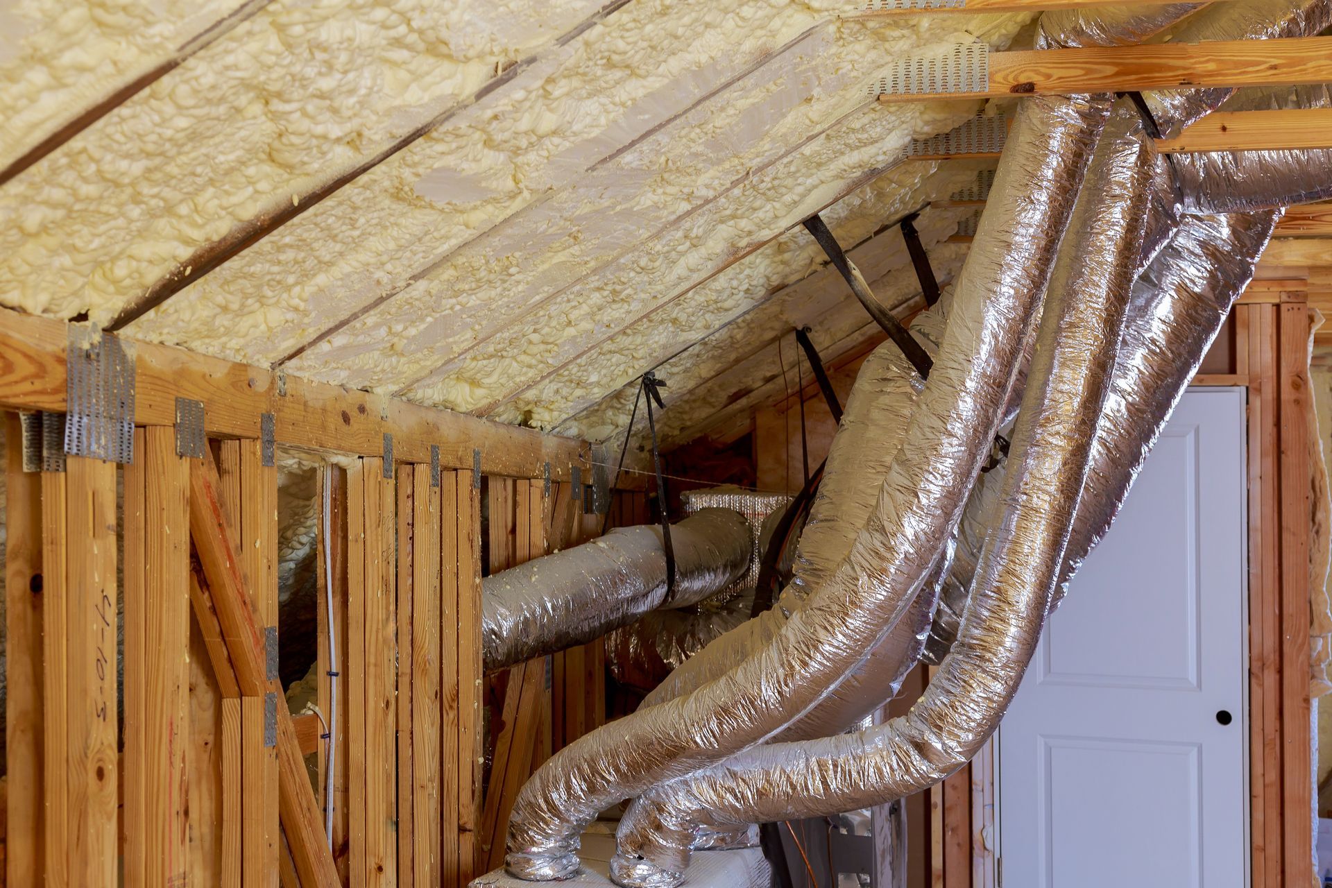 Wooden house frame with silver ductwork and insulation in attic.