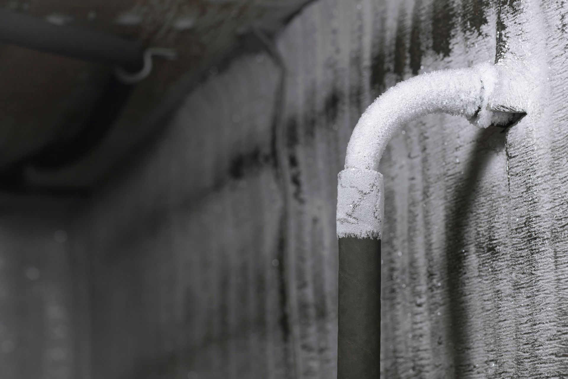 A close up of a pipe covered in frost on a wall.