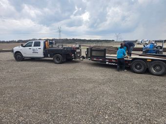 White tow truck with flatbed trailer and workers on a gravel lot under a cloudy sky