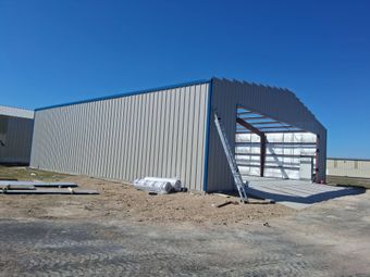 Industrial building under construction with corrugated metal walls and open front framing.
