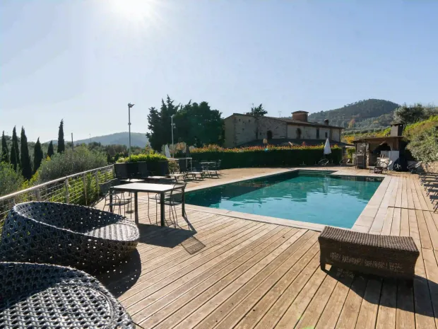 Una piscina all'aperto baciata dal sole su una terrazza in legno in un paesaggio toscano, con lettini prendisole e un set da pranzo.