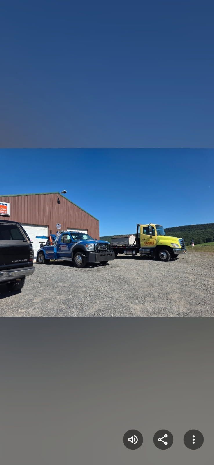 Two tow trucks parked in front of a building on a gravel lot under a blue sky.