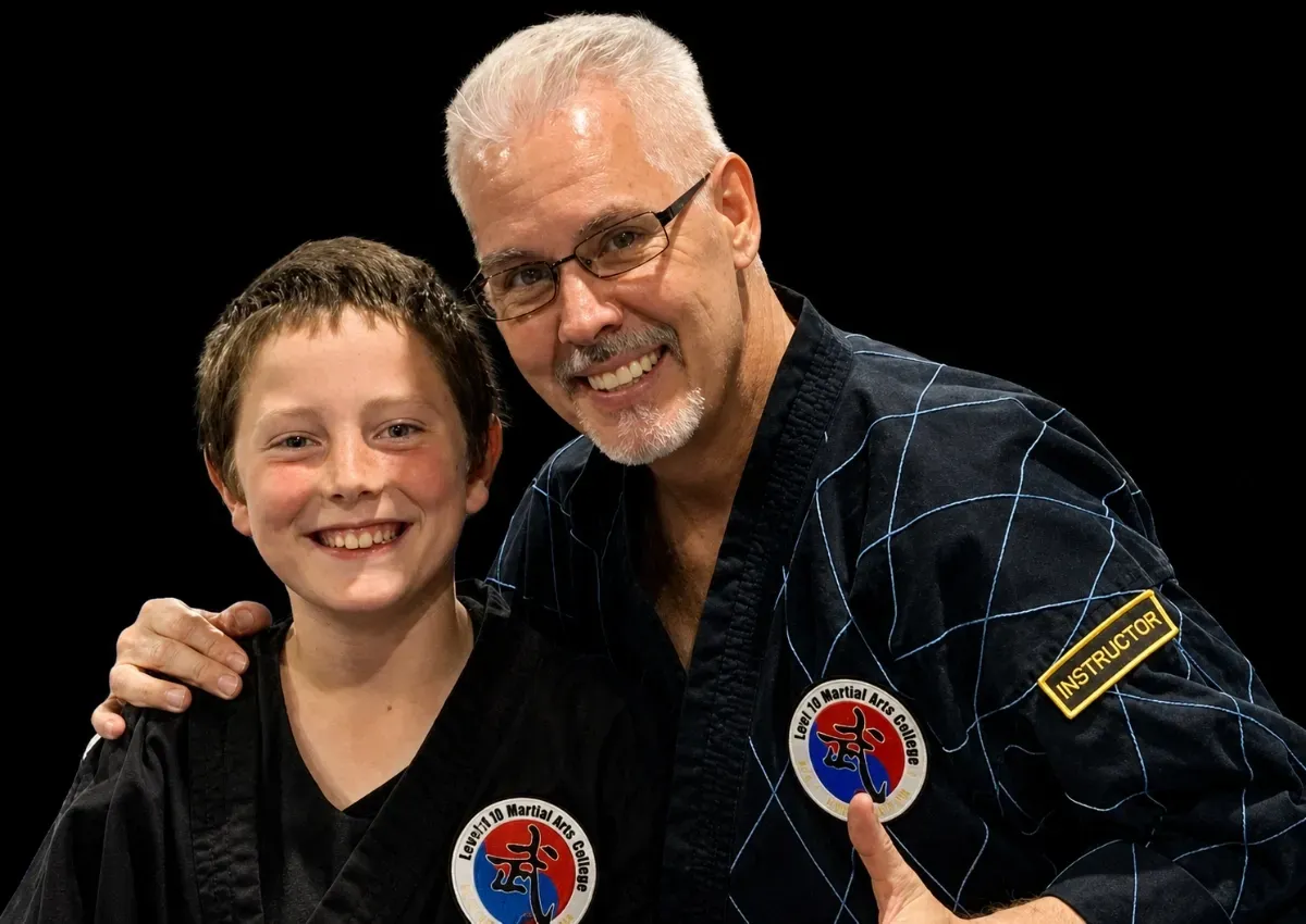 Two smiling martial arts students in black uniforms with patches, posing together against a black background