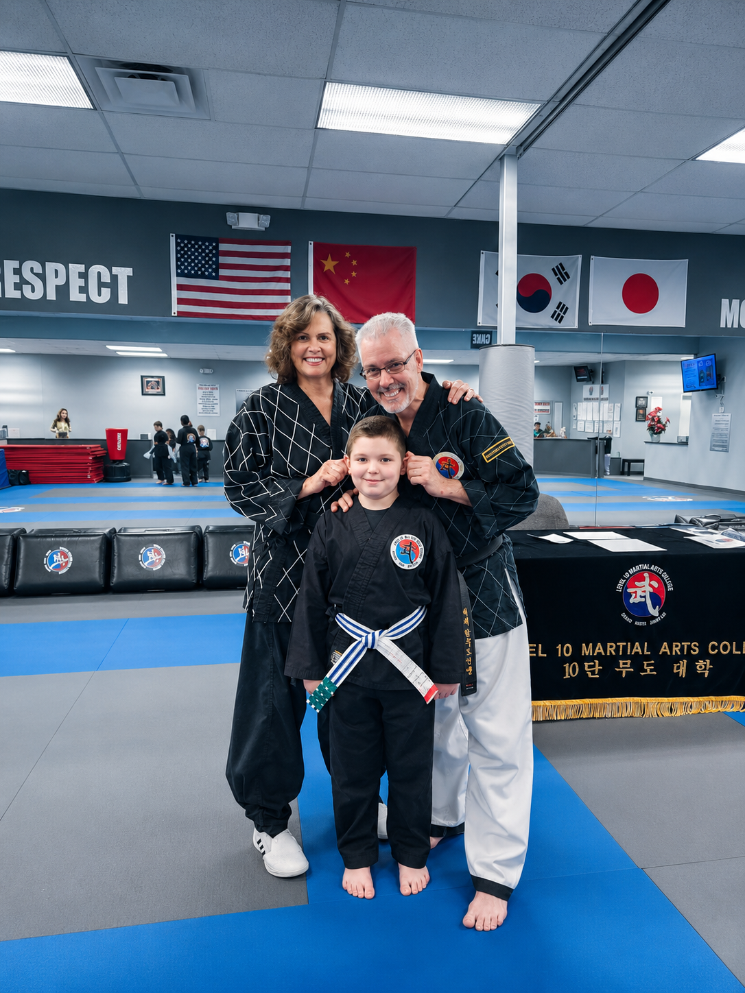 Three people posing in a martial arts studio, with a child in a black gi and white belt in front.