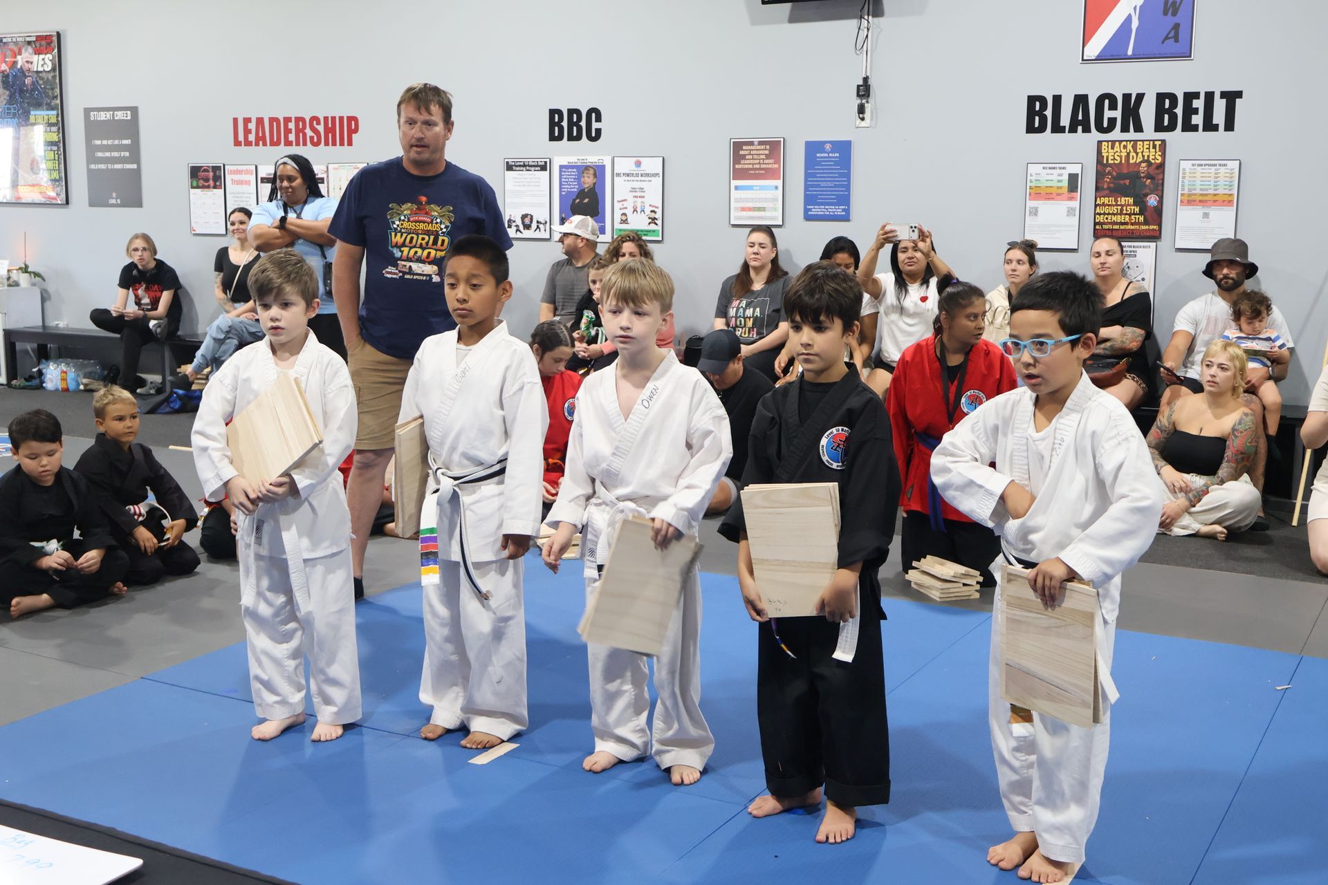 Children in martial arts uniforms lined up in a dojo, holding belts during a belt ceremony.