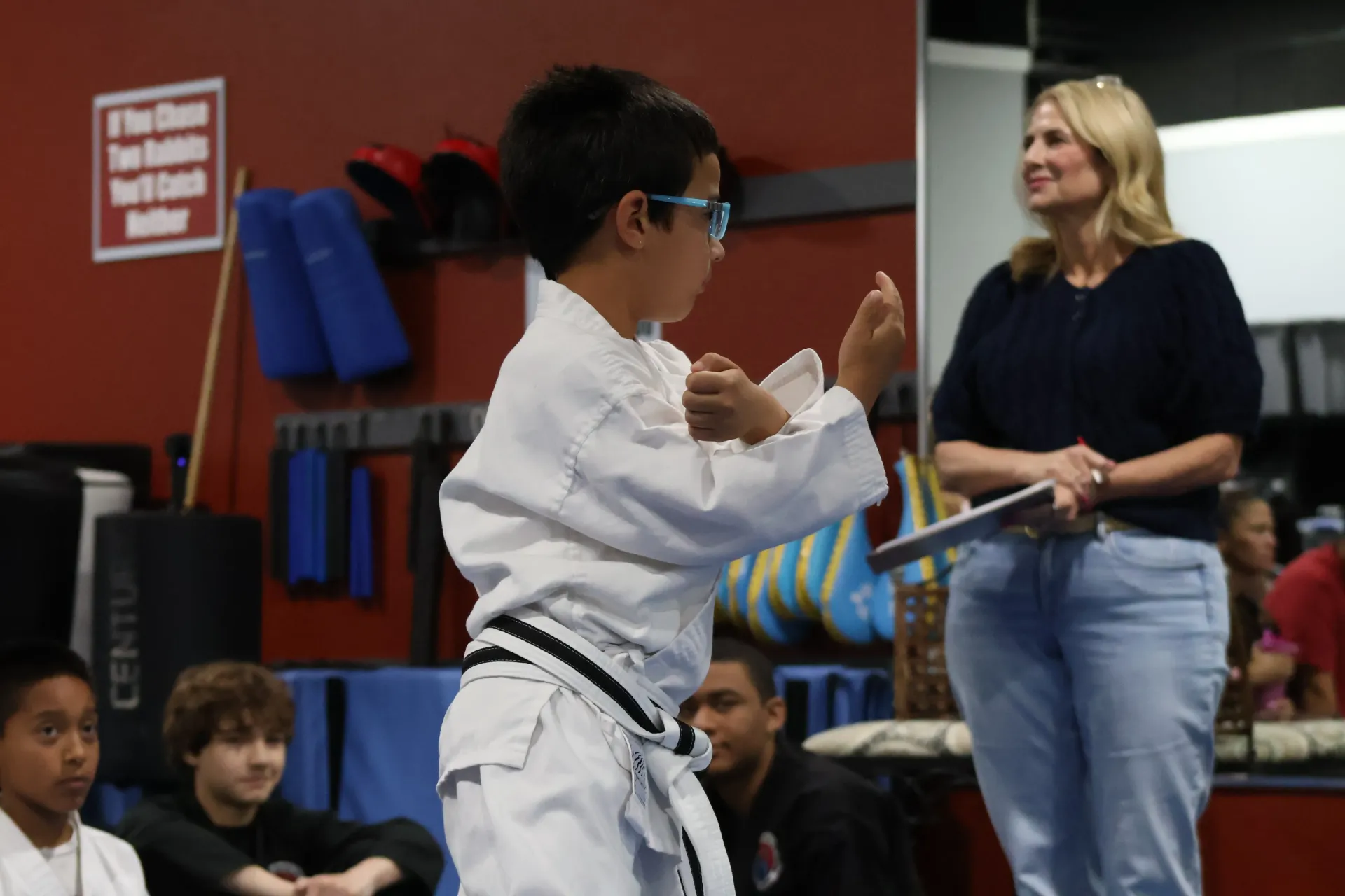 Martial arts student in white gi sparring indoors while an instructor watches nearby