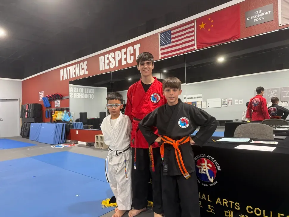 Three martial arts students posing in a dojo with blue mats and wall banners behind them