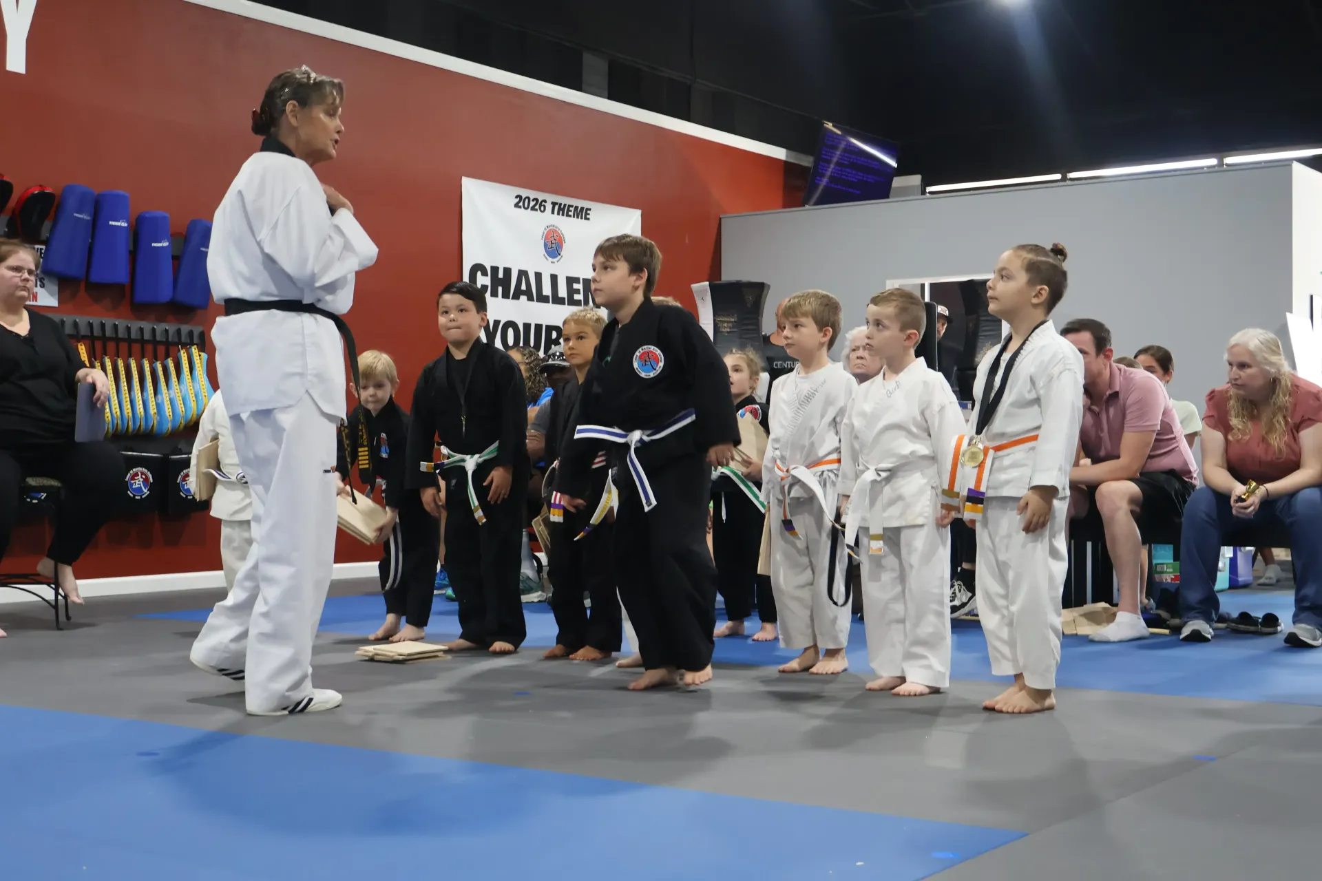 Martial arts instructor addressing children in gis at a tournament on a blue mat