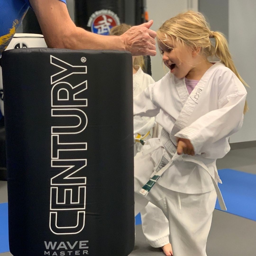 A group of children are practicing karate with a teacher in a gym.