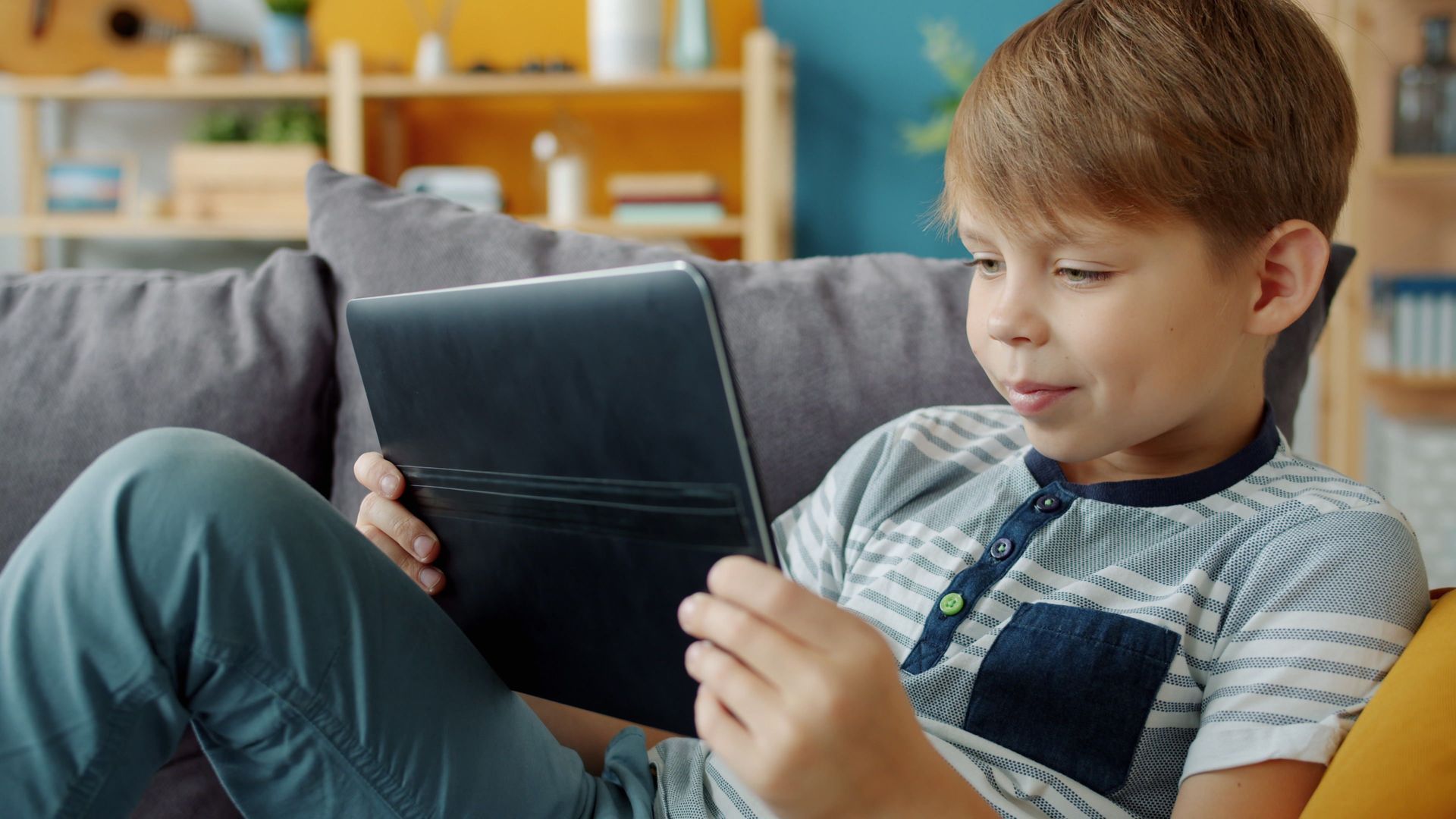 Child sitting on a couch, looking at a tablet in a cozy living room.