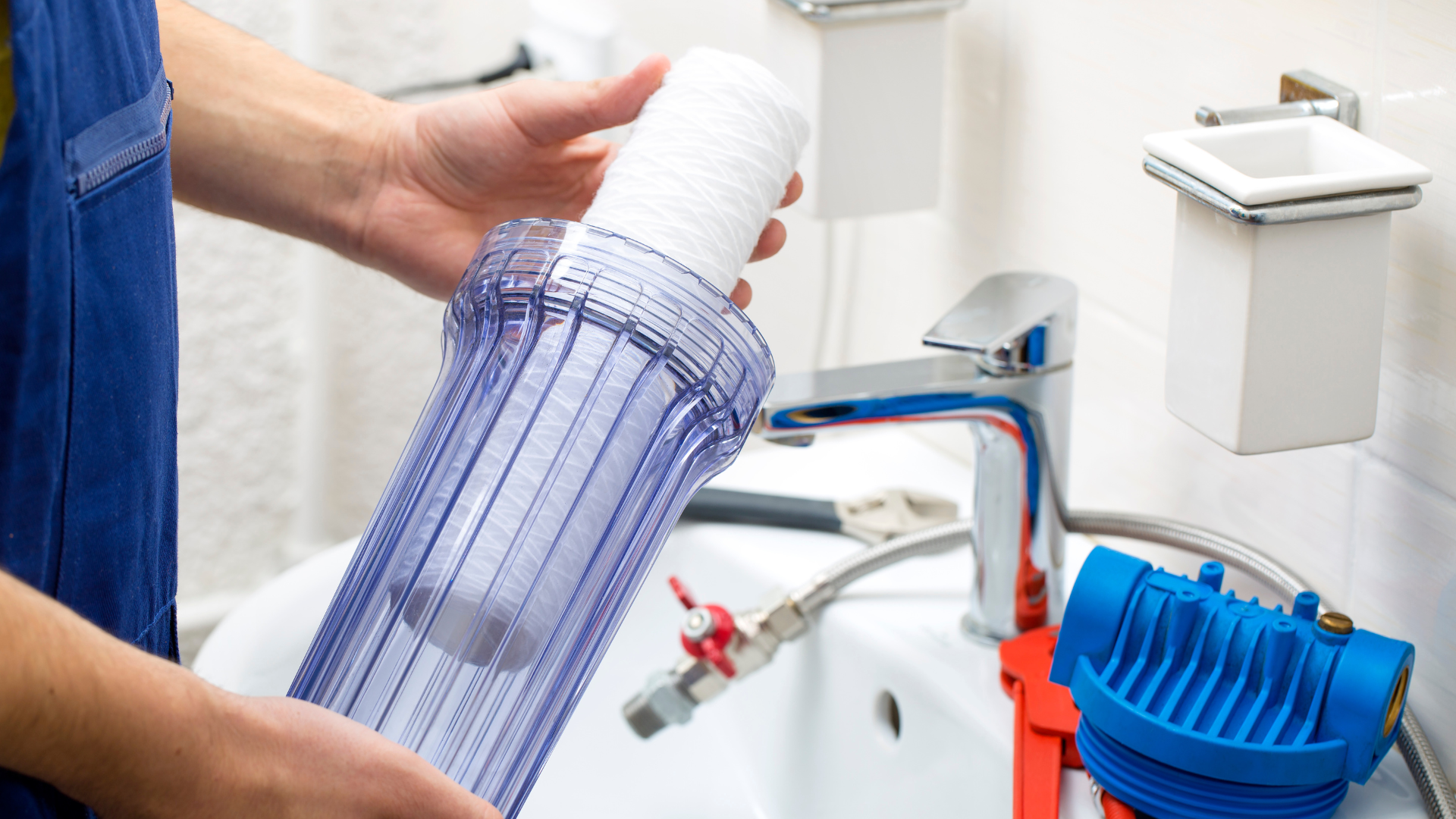 A person is holding a water filter in front of a sink.