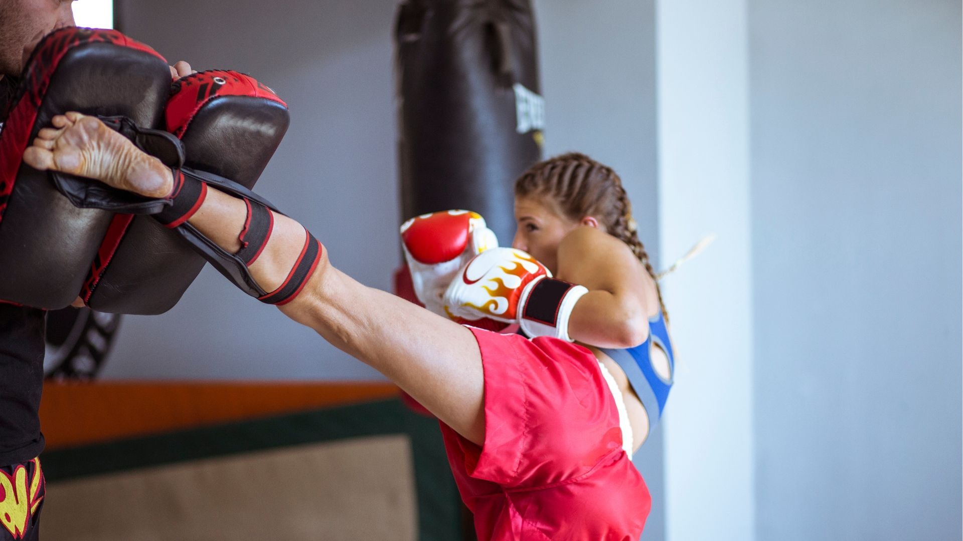 A woman at a Kickboxing Class executing a well-timed kick on a piece of equipment.