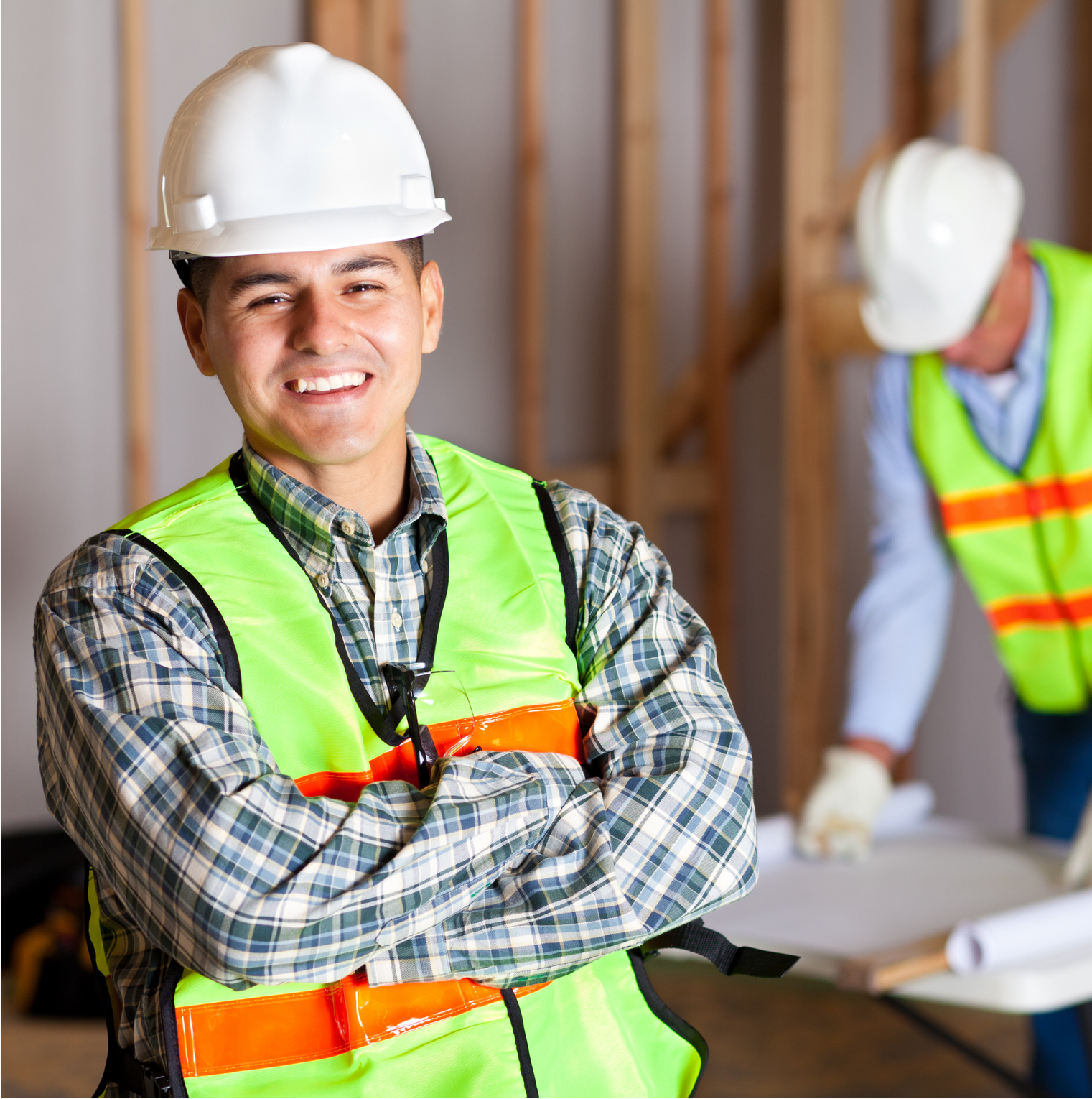 A man wearing a hard hat and safety vest is smiling with his arms crossed