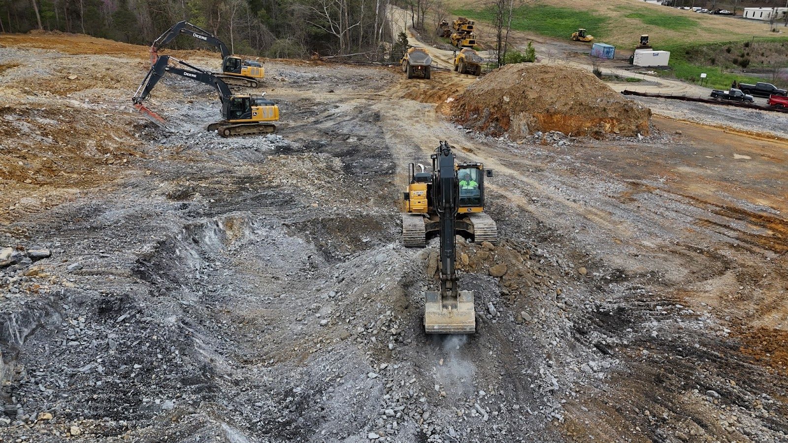 A group of construction vehicles are working on a dirt road.