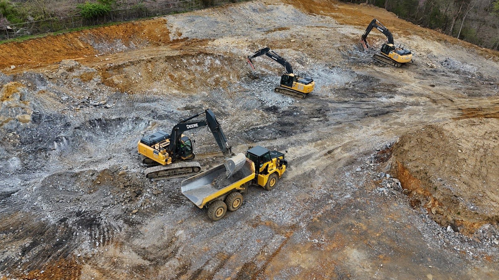 A group of construction vehicles are working on a dirt field.