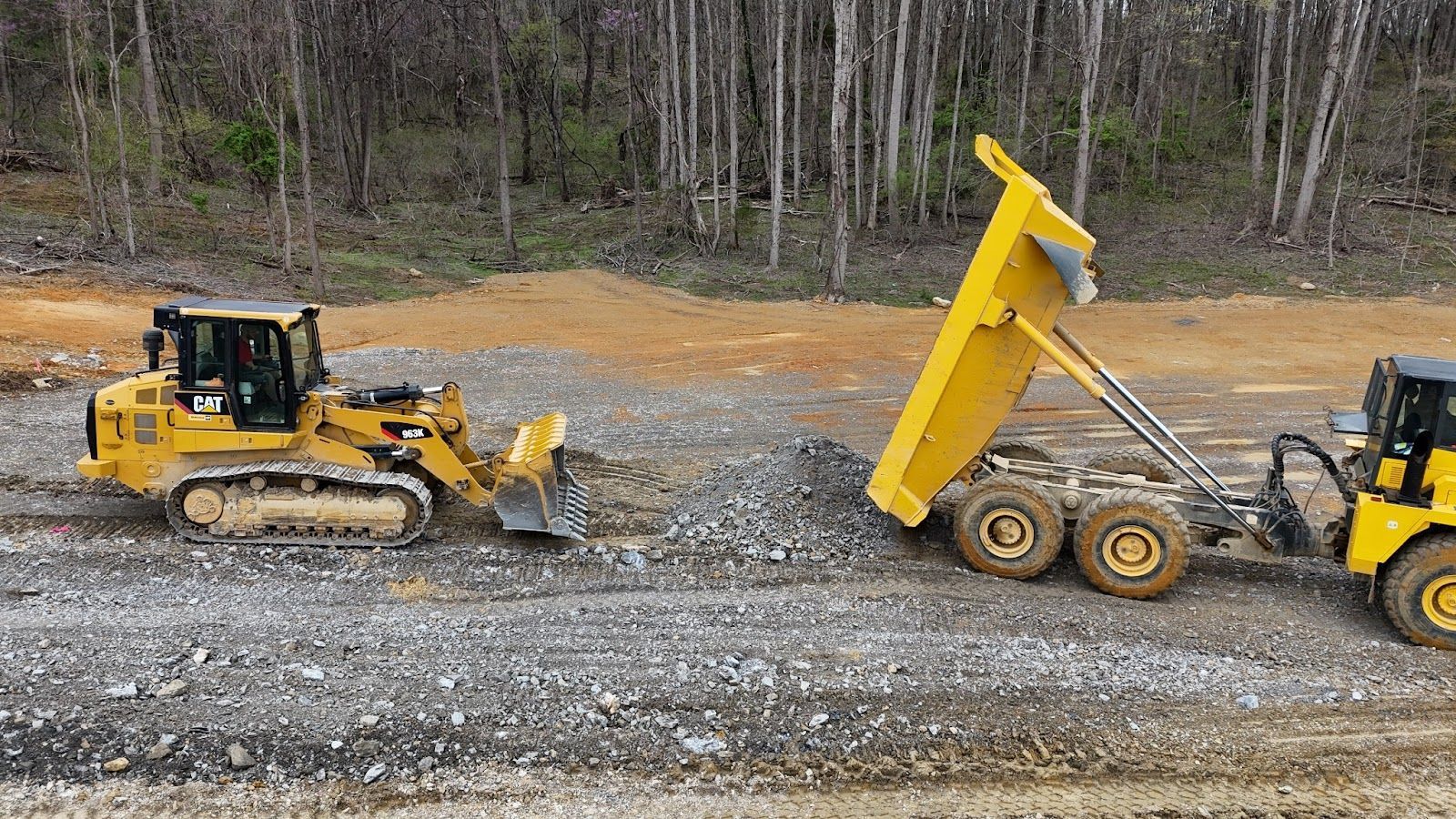 A dump truck is being towed by a bulldozer on a dirt road.