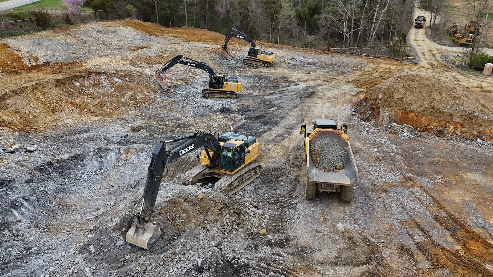 A group of construction vehicles are working on a dirt road.