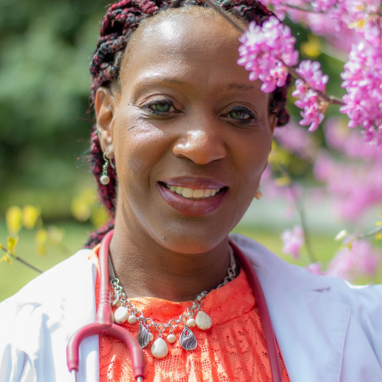 Nurse Linda A. Gilliam-Johnson standing amidst purple flowers with a stethoscope in an orange dress and white lab coat