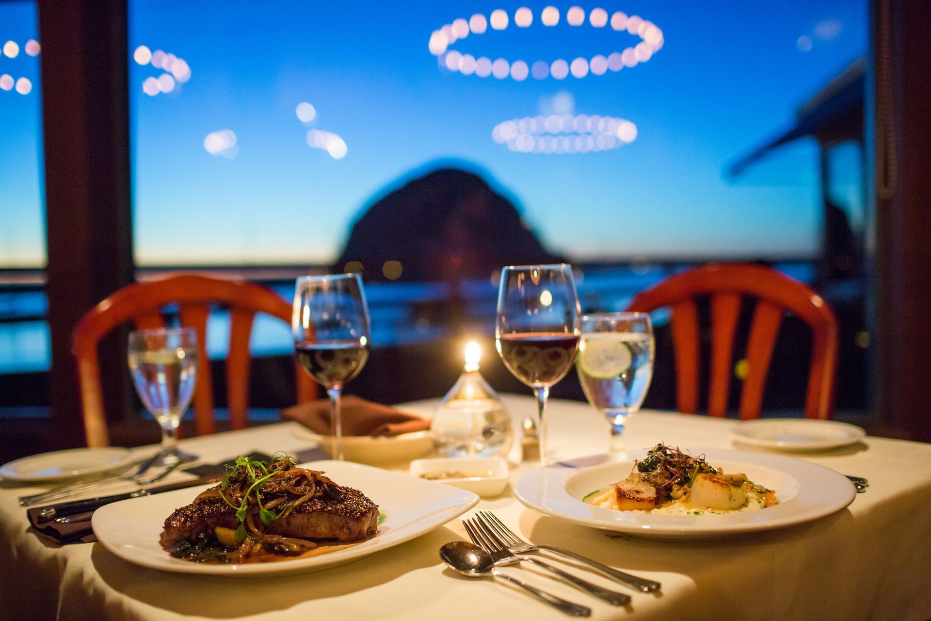 Two plates of food and two glasses of wine are on a table.