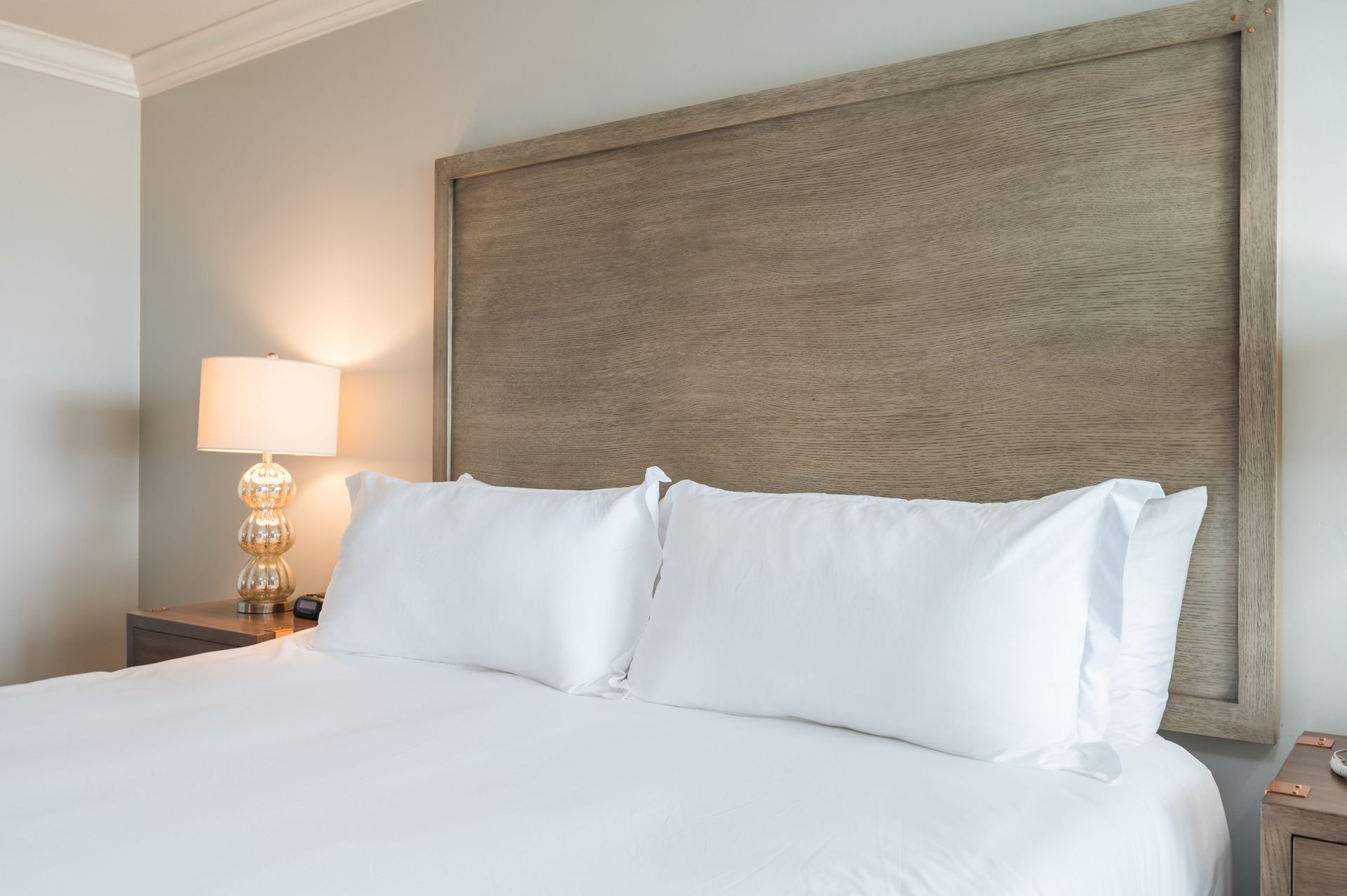 A hotel room with a bed , nightstand , lamp and wooden headboard.