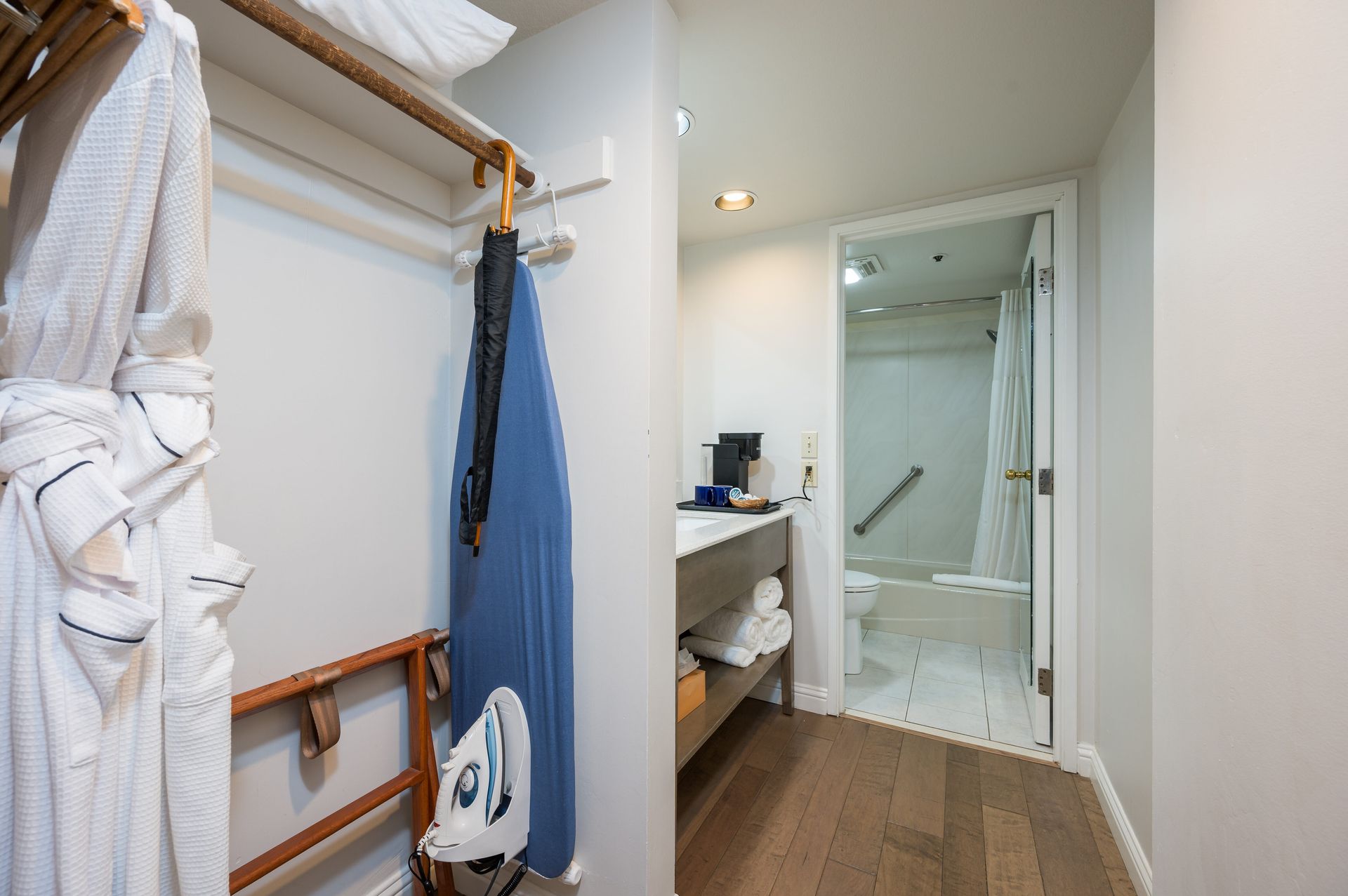 A hotel room with a robe hanging on the wall and an ironing board hanging on the wall.