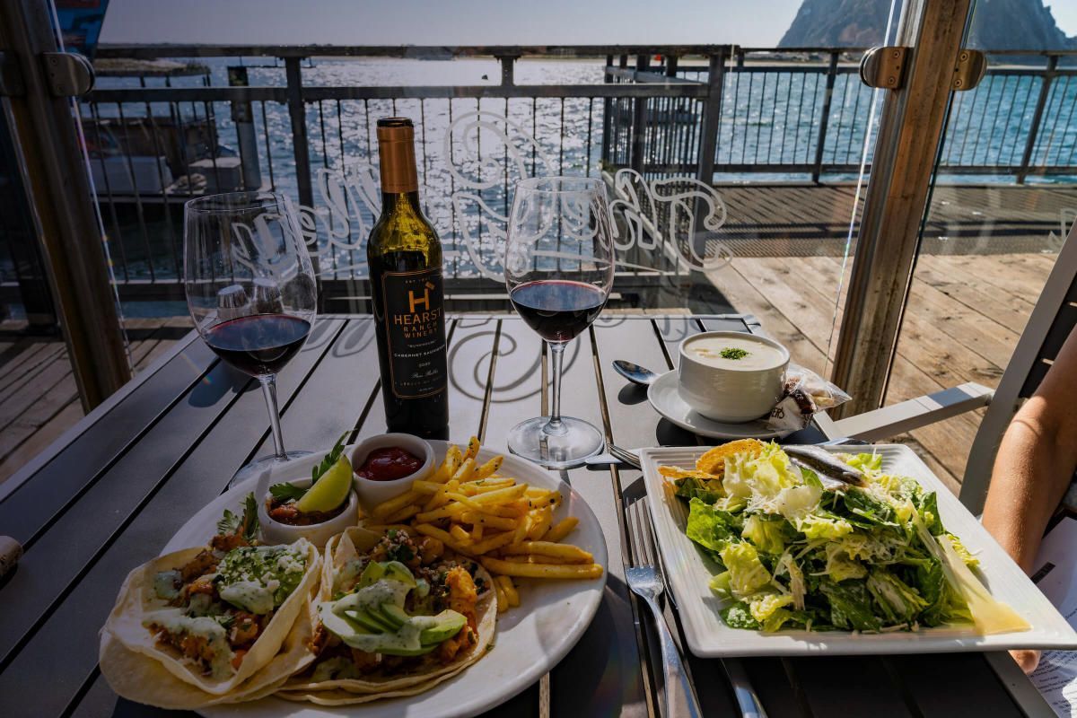 A person is sitting at a table with a plate of food and a bottle of wine.