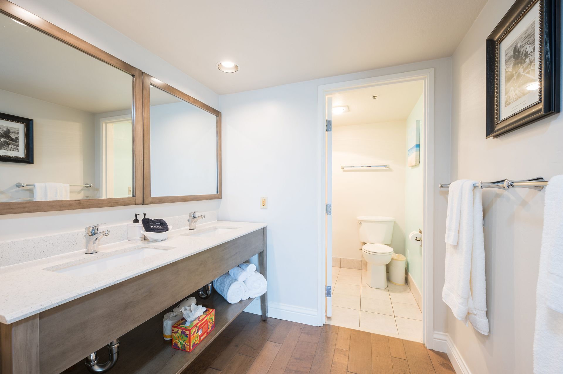 A bathroom with two sinks , two mirrors and a toilet.