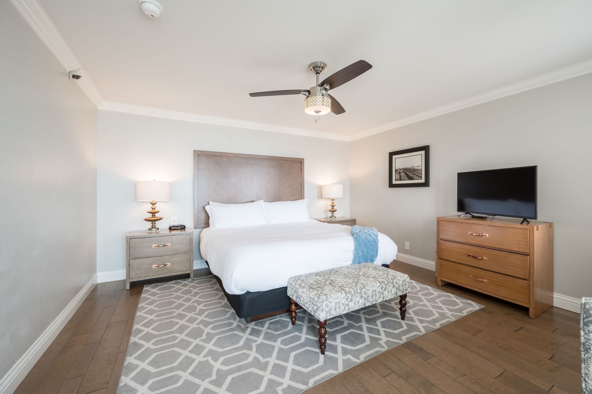 A bedroom with a king size bed , dresser , television and ceiling fan.