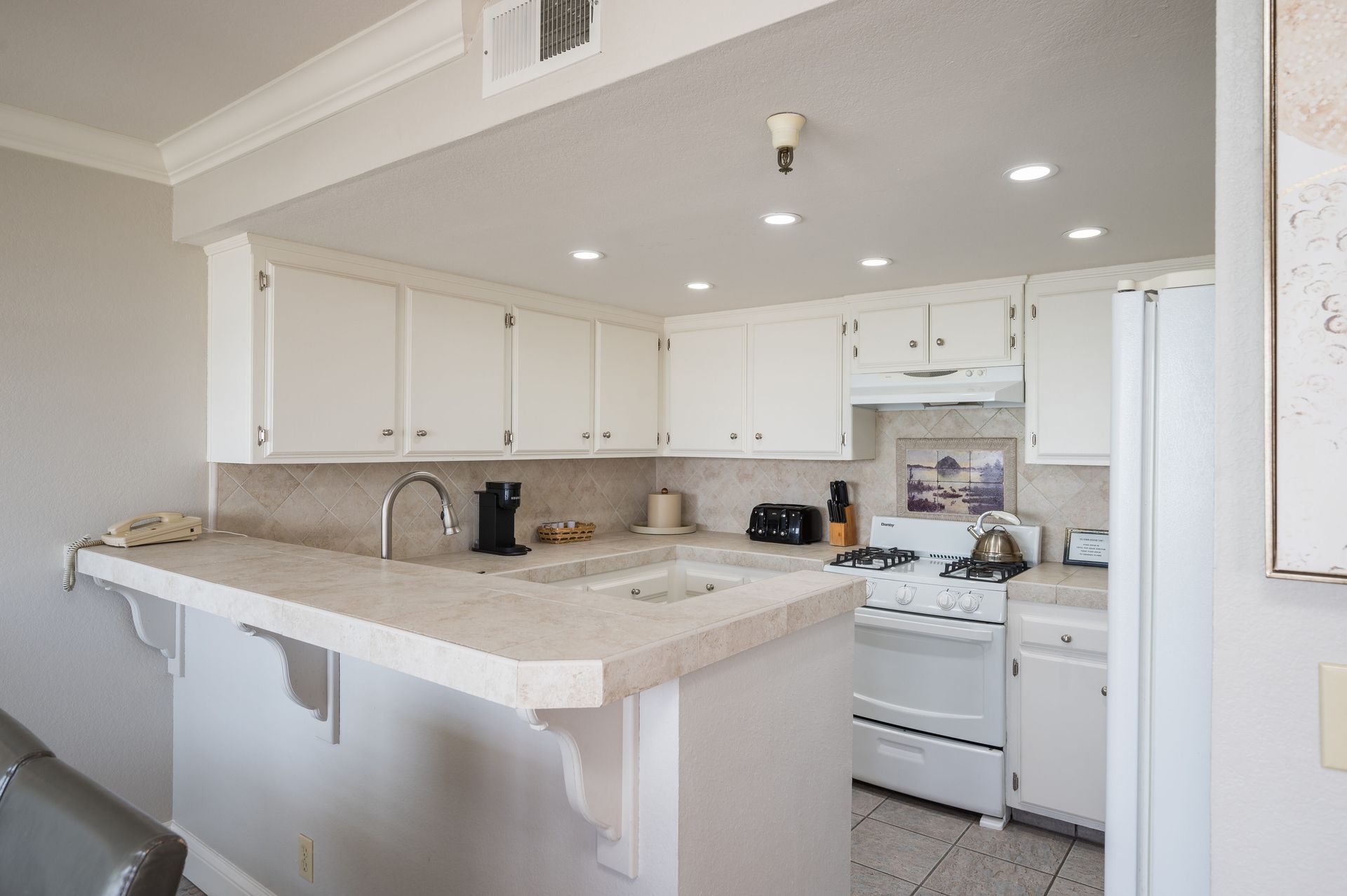 A kitchen with white cabinets , a stove , a sink , and a refrigerator.