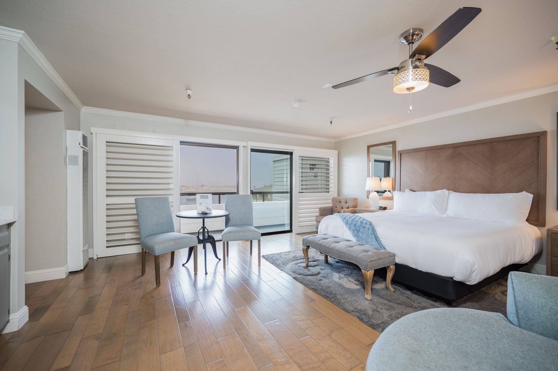 A hotel room with a king size bed , chairs , a table and a ceiling fan.