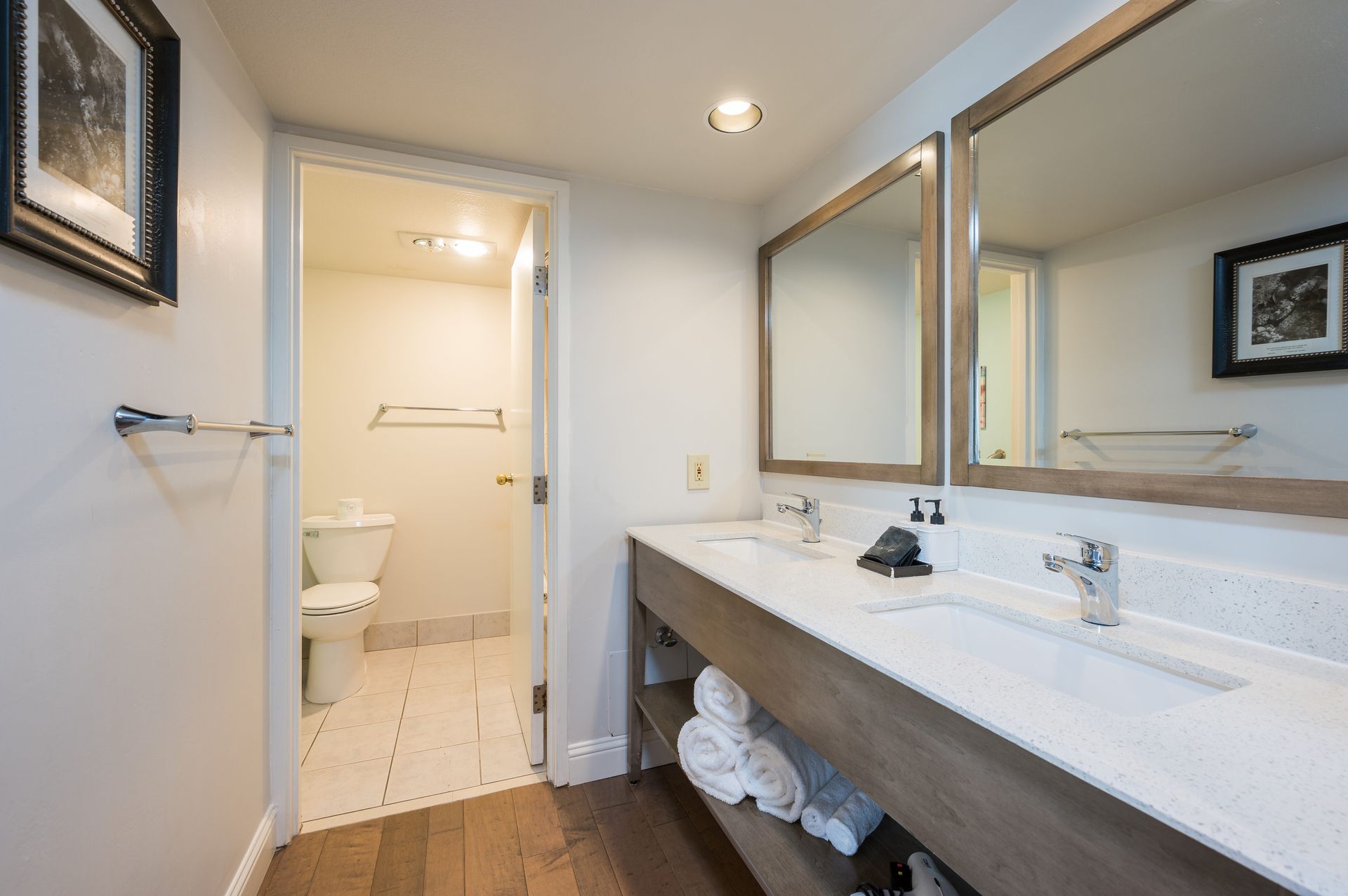 A bathroom with two sinks , two mirrors and a toilet.