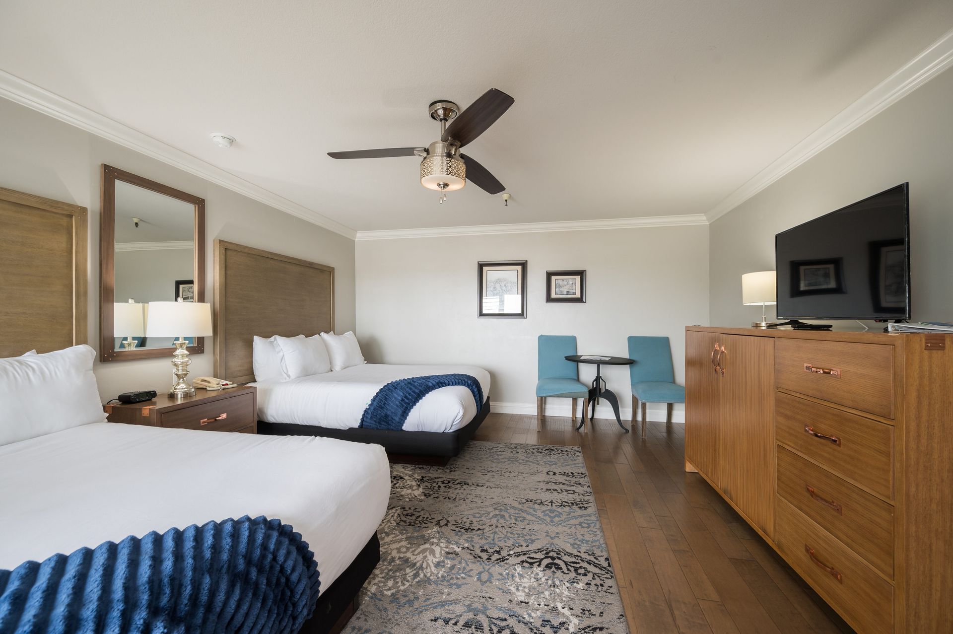 A hotel room with two beds , a ceiling fan , a table and chairs.