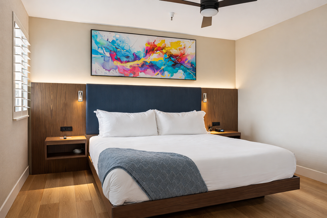 A bedroom with a king size bed , dresser , television and ceiling fan.