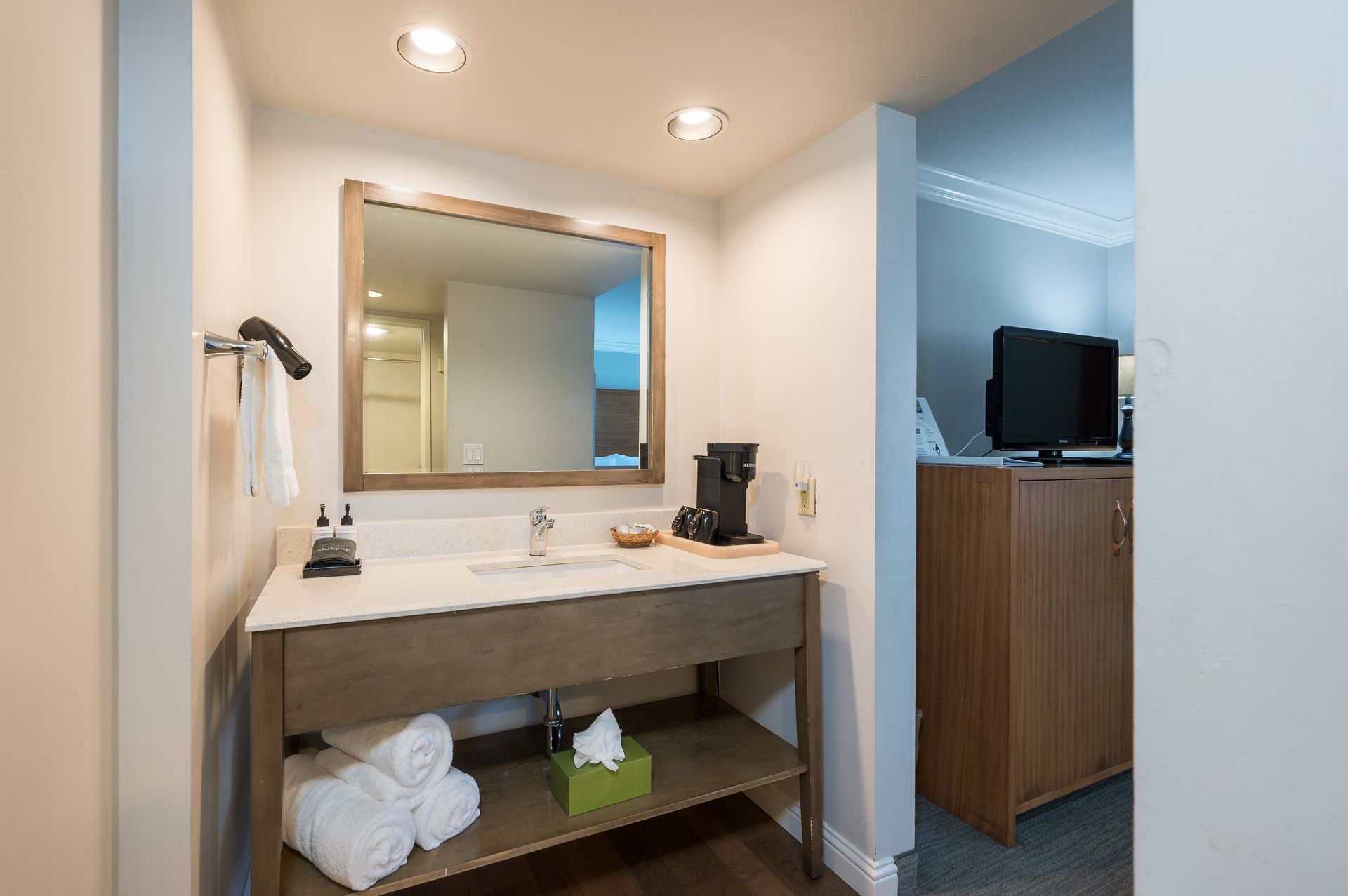 A bathroom in a hotel room with a sink , mirror and towels.